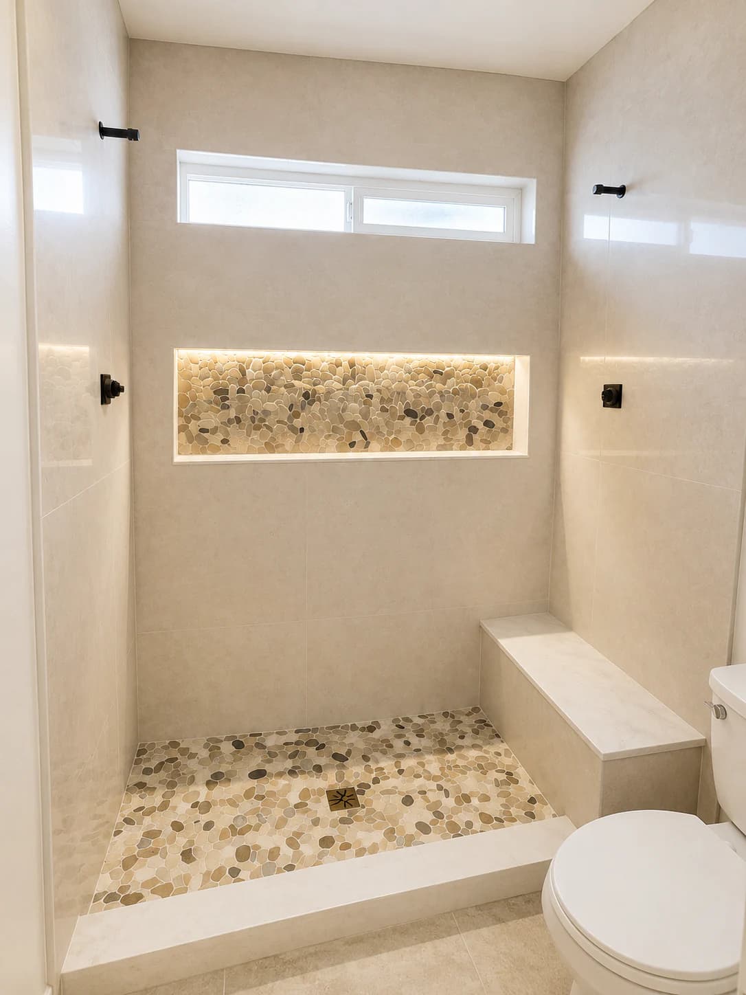 Finished light-toned shower with an illuminated pebble niche and built-in bench