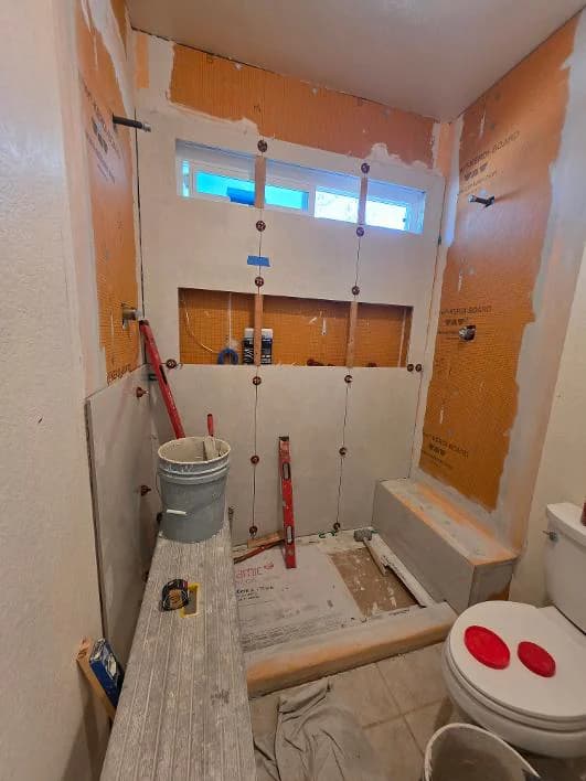 Shower tile installation in progress with leveling clips, a bucket, and a level