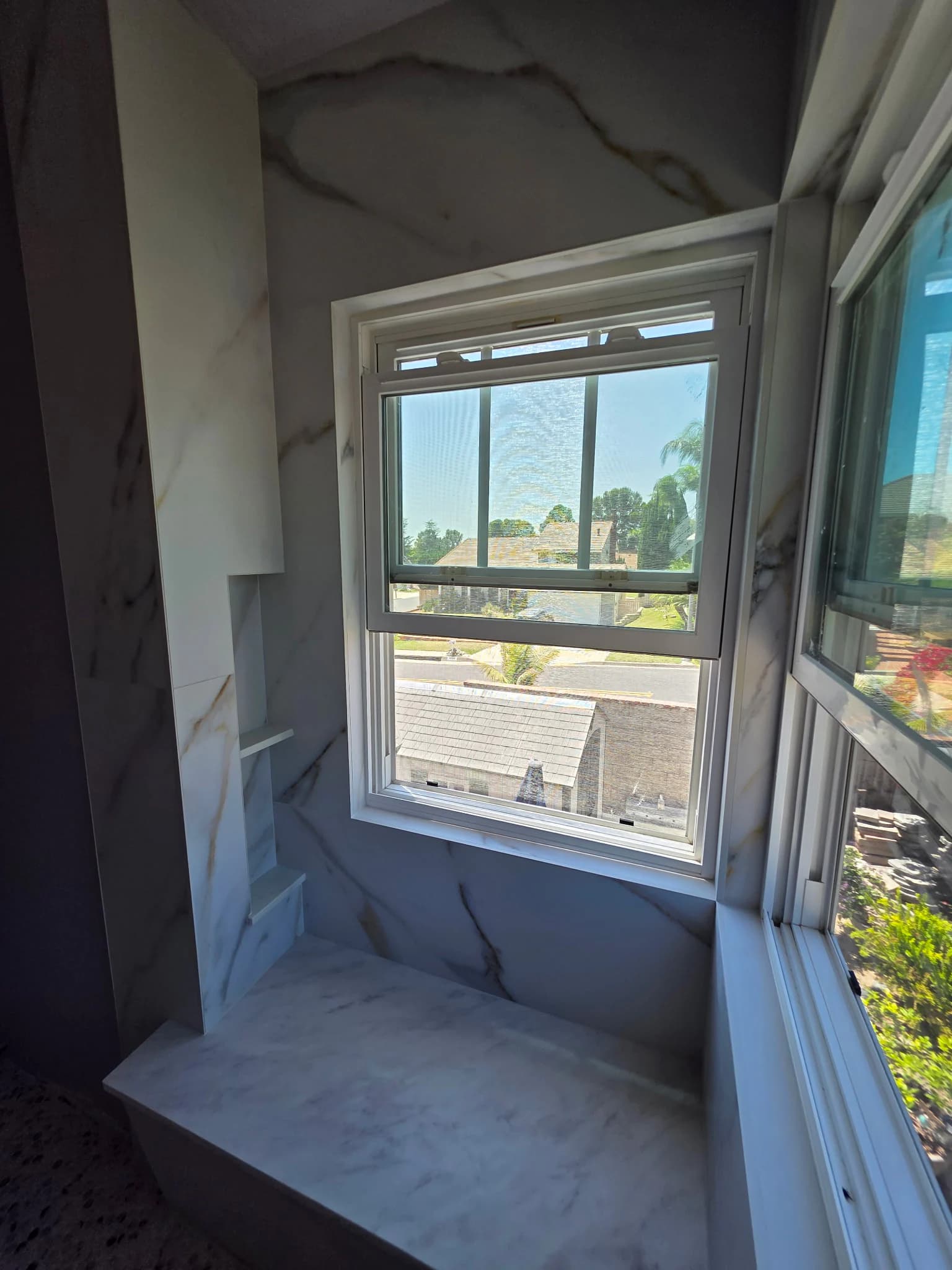 Marble-look tile detailing around a shower bench and corner windows