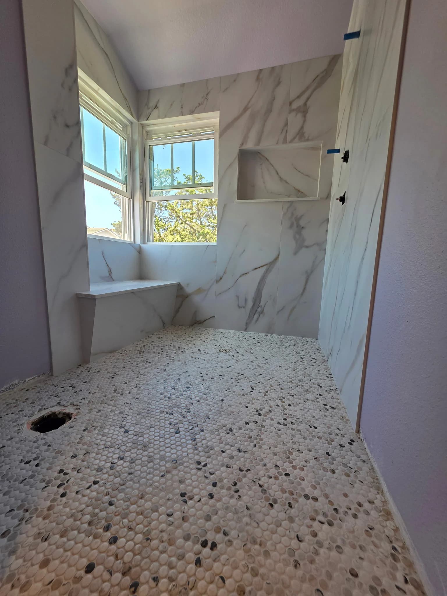 Near-finished marble-look shower with a built-in bench and pebble floor