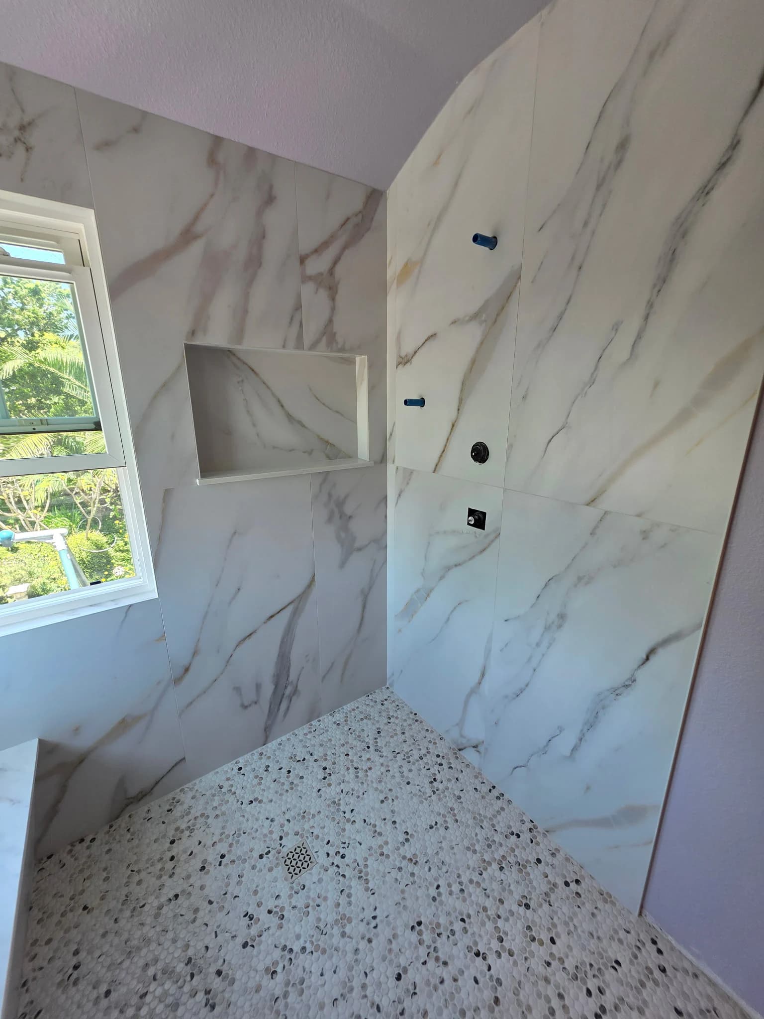Recessed shower niche with marble-look wall tile and pebble mosaic floor