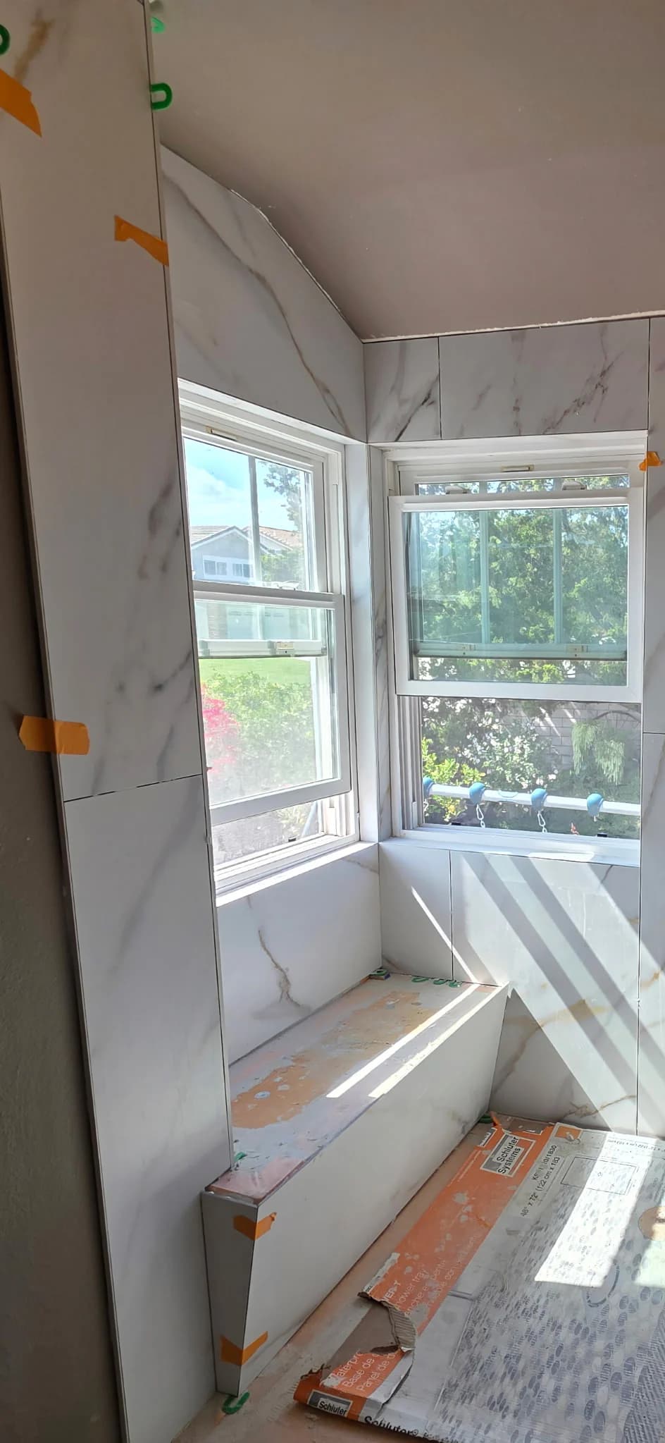 Marble-look tile installation in progress around two shower windows